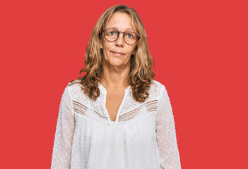 Middle age blonde woman wearing casual white shirt and glasses relaxed with serious expression on face. simple and natural looking at the camera.