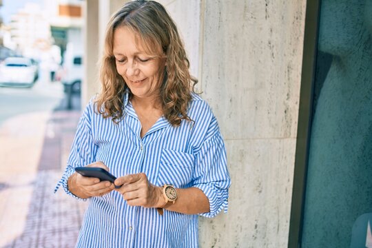 Middle age caucasian woman smiling happy using smartphone at the city.