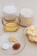 Glass of flour, glass of powdered sugar, pieces of butter, spices and honey on tablecloth. Ingredients for cooking.