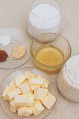 Glass of flour, glass of powdered sugar, pieces of butter, spices and honey on tablecloth. Ingredients for cooking.