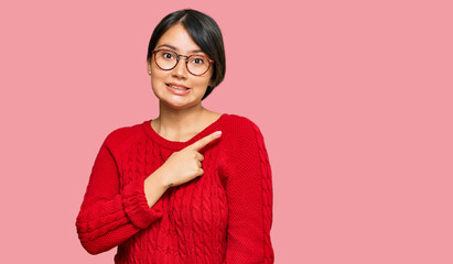 Young beautiful hispanic woman with short hair wearing casual sweater and glasses pointing aside...