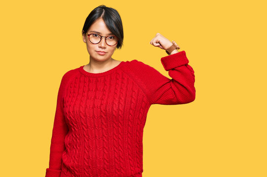 Young beautiful hispanic woman with short hair wearing casual sweater and glasses strong person showing arm muscle, confident and proud of power