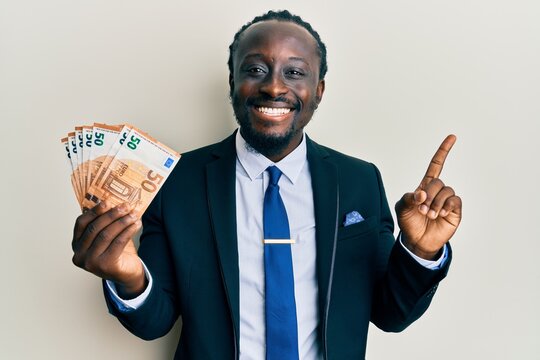 Handsome young black man wearing business suit holding 50 euros banknotes smiling happy pointing with hand and finger to the side