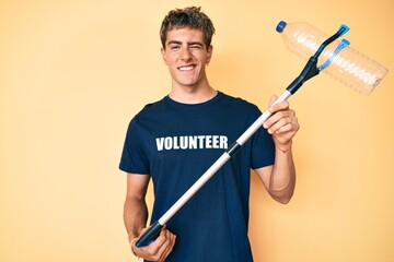 Young handsome man recycling plastic bottle holding litter pick up tool winking looking at the...