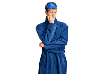 Young handsome man wearing sleep mask and bathrobe looking stressed and nervous with hands on mouth biting nails. anxiety problem.