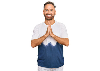 Handsome middle age man wearing casual tie dye tshirt praying with hands together asking for forgiveness smiling confident.