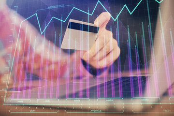 Double exposure of man hands holding a credit card and Forex graph drawing. Stock trading and digital fintech in Internet E-commerce concept.