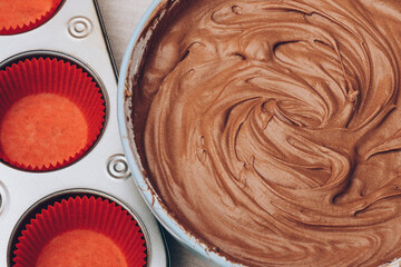 Cacao dough for cupcakes, red paper molds and metal baking tray on tablecloth. Preparing process to baking. Top view.