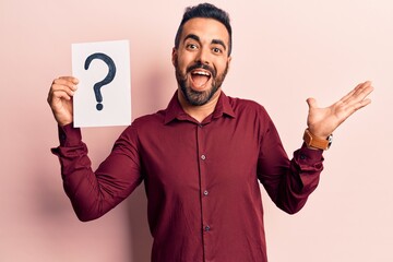 Young hispanic man holding question mark celebrating achievement with happy smile and winner expression with raised hand