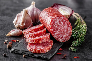 Traditional smoked salami sausage with spices.Salami sausage slices on a black chopping Board. Dark background.