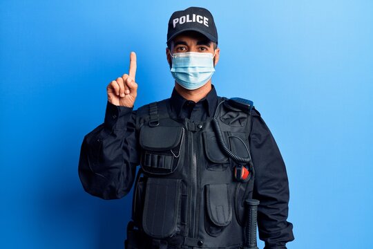 Young hispanic man wearing police uniform and medical mask smiling with an idea or question pointing finger up with happy face, number one