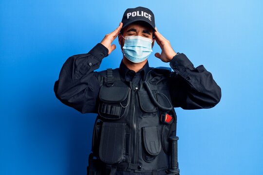 Young hispanic man wearing police uniform and medical mask with hand on head, headache because stress. suffering migraine.