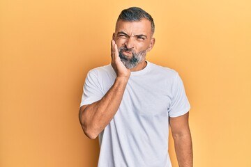 Middle age handsome man wearing casual white tshirt touching mouth with hand with painful expression because of toothache or dental illness on teeth. dentist