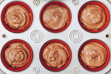 Cacao dough for cupcakes in red paper molds in metal baking tray close-up. Preparing process to baking. Top view.
