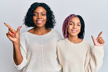 Beautiful african american mother and daughter wearing casual clothes and hugging cheerful with a smile on face pointing with hand and finger up to the side with happy and natural expression