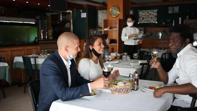 female waitress in mask taking order from female and male customers in cafe 