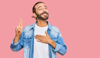 Attractive man with long hair and beard wearing casual denim jacket smiling swearing with hand on...