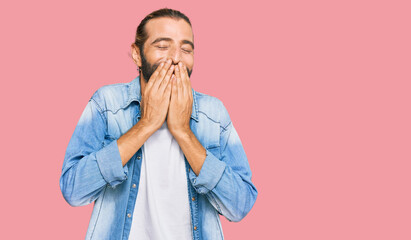 Attractive man with long hair and beard wearing casual denim jacket laughing and embarrassed giggle...