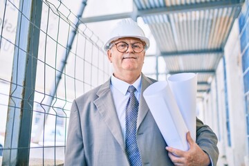Fototapeta premium Senior grey-haired architect man holding blueprints walking at street of city