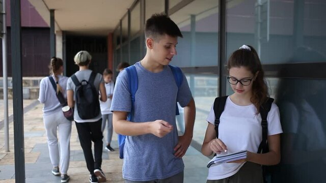 Focused teen boy talking to girl classmate outdoors in college campus, discussing schoolwork