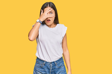 Young caucasian woman wearing casual white tshirt peeking in shock covering face and eyes with hand, looking through fingers with embarrassed expression.