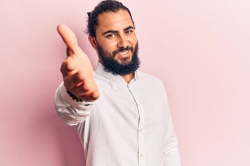 Naklejka premium Young arab man wearing casual clothes smiling friendly offering handshake as greeting and welcoming. successful business.