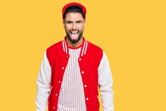 Young man with beard wearing baseball uniform sticking tongue out happy with funny expression. emotion concept.