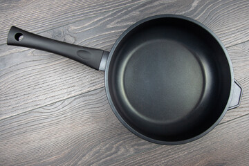 Biack frying pan with non-stick teflon coating on wooden background