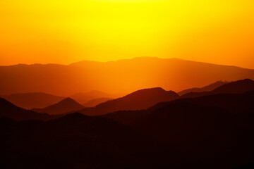 Beautiful sunset or sunrise colors over the mountains. Majestic colorful landscape in the mountains. Dramatic dark orange and red mountain landscape with fog.