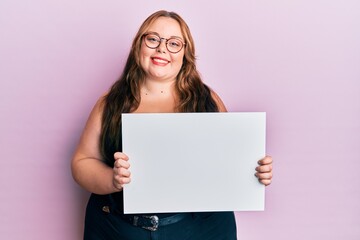 Plus size caucasian young woman holding blank empty banner looking positive and happy standing and smiling with a confident smile showing teeth