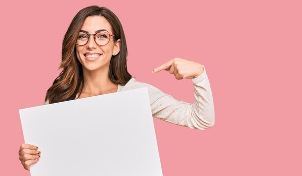 Young brunette woman holding blank empty banner pointing finger to one self smiling happy and proud