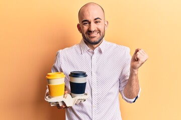 Young handsome bald man holding cup of takeaway coffee screaming proud, celebrating victory and success very excited with raised arm