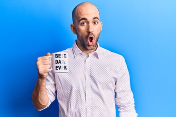 Young handsome bald man drinking cup of coffee with best dad ever message scared and amazed with open mouth for surprise, disbelief face