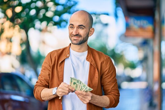 Young hispanic bald man smiling happy counting usa dollars at the city.