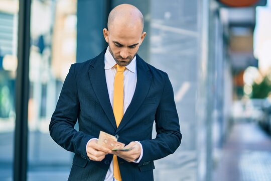 Young hispanic bald businessman with serious expression counting canadian dollars banknotes at the city.
