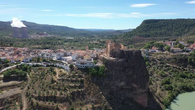 Aerial view of historical Spanish town of Cofrentes with medieval castle on top of basalt rock and modern nuclear power plant cooling towers on background, Valencia, Spain. High quality 4k footage