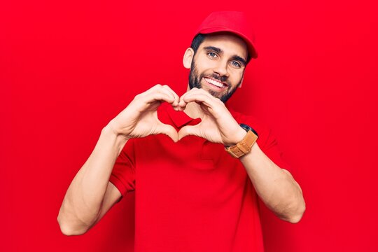 Young handsome man with beard wearing casual polo and cap smiling in love doing heart symbol shape with hands. romantic concept.