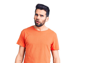 Fototapeta premium Young handsome man with beard wearing casual t-shirt in shock face, looking skeptical and sarcastic, surprised with open mouth