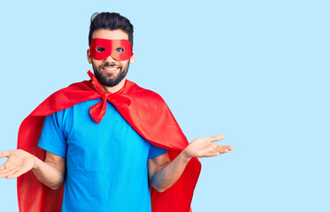 Young handsome man with beard wearing super hero costume clueless and confused expression with arms...