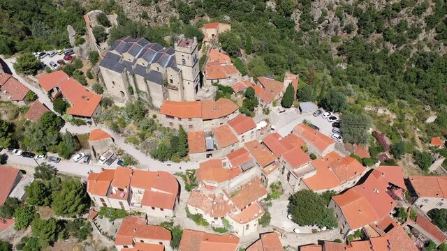 Scenic aerial view of compact village of Eus on green slopes of hill with ancient church of St. Vincent and stone castle ruins on hilltop, France