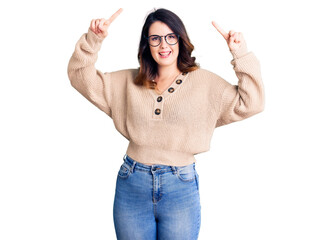 Beautiful young brunette woman wearing casual clothes and glasses smiling amazed and surprised and pointing up with fingers and raised arms.