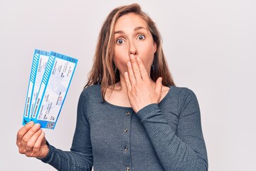 Young beautiful blonde woman holding boarding pass covering mouth with hand, shocked and afraid for...