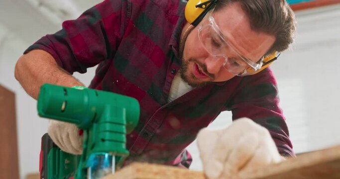 Young smiling carpenter cuts osb board with jigsaw in carpentry workshop. The hands of a craftsman wearing protective cloth gloves. The jigsaw blade cuts precisely.