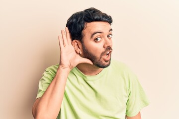 Young hispanic man wearing casual clothes smiling with hand over ear listening and hearing to rumor or gossip. deafness concept.