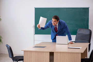 Young male teacher in suit in front of green board