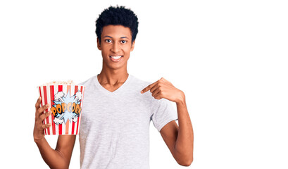 Young african american man holding popcorn pointing finger to one self smiling happy and proud