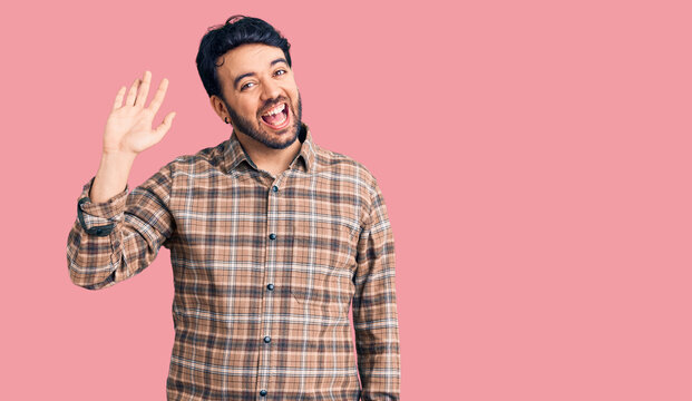 Young hispanic man wearing casual clothes waiving saying hello happy and smiling, friendly welcome gesture