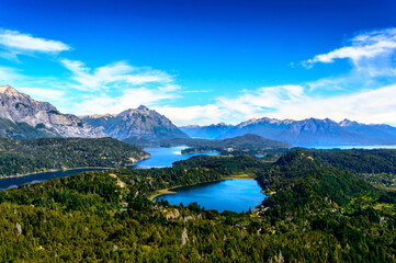 Fototapeta na wymiar Beautiful lake landscape in the middle of mountains surrounded by pine trees and rocks everywhere. Very sunny day in the mountain of Bariloche. Green foliage and huge rocks.