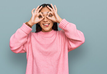 Young asian woman wearing casual winter sweater doing ok gesture like binoculars sticking tongue out, eyes looking through fingers. crazy expression.