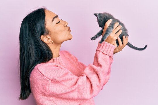 Young hispanic girl smiling happy holding cute cat over isolated pink background.